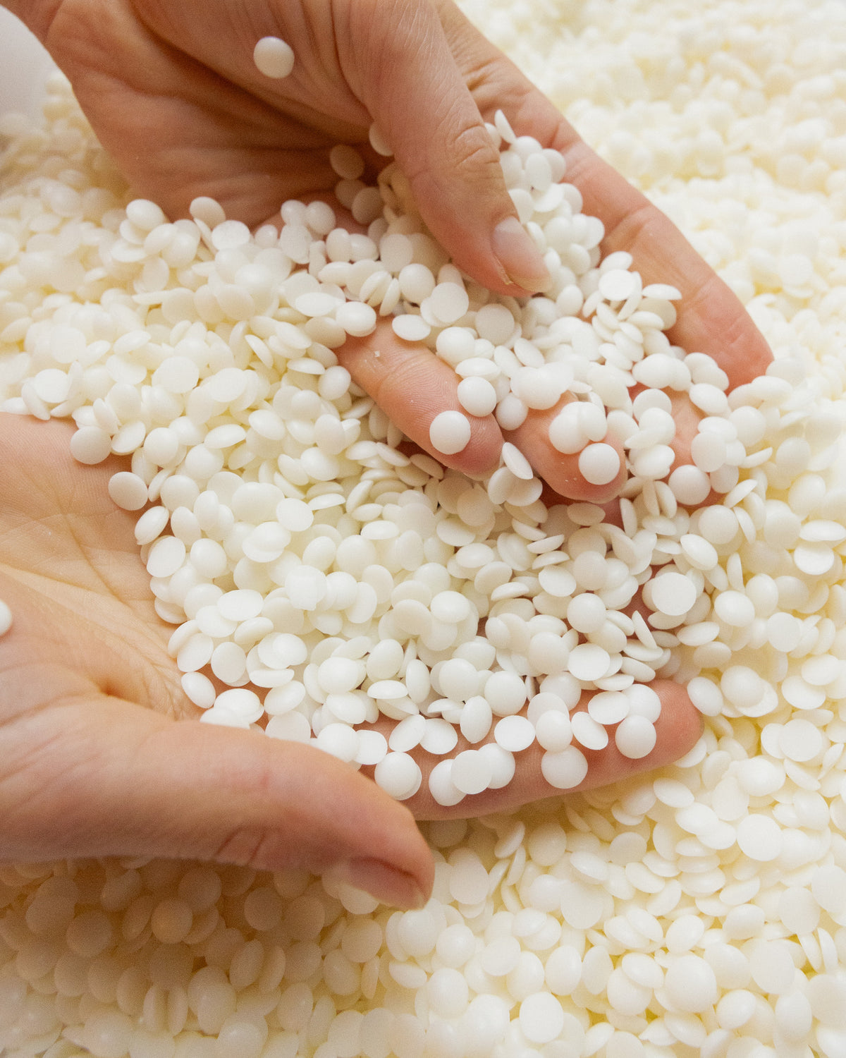 Beeswax and soy wax pellets held in two hands, the material Pillar Candle II is cast from