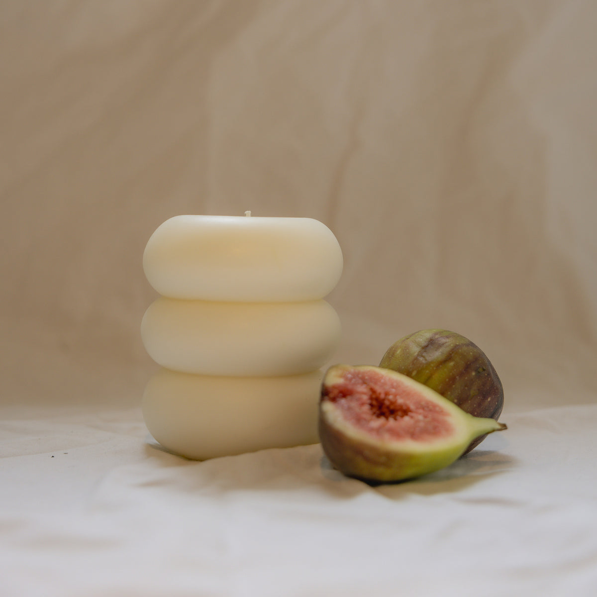 Pillar Candle I, a three tier sculptural candle in beeswax and soy, unscented, beside a fresh fig