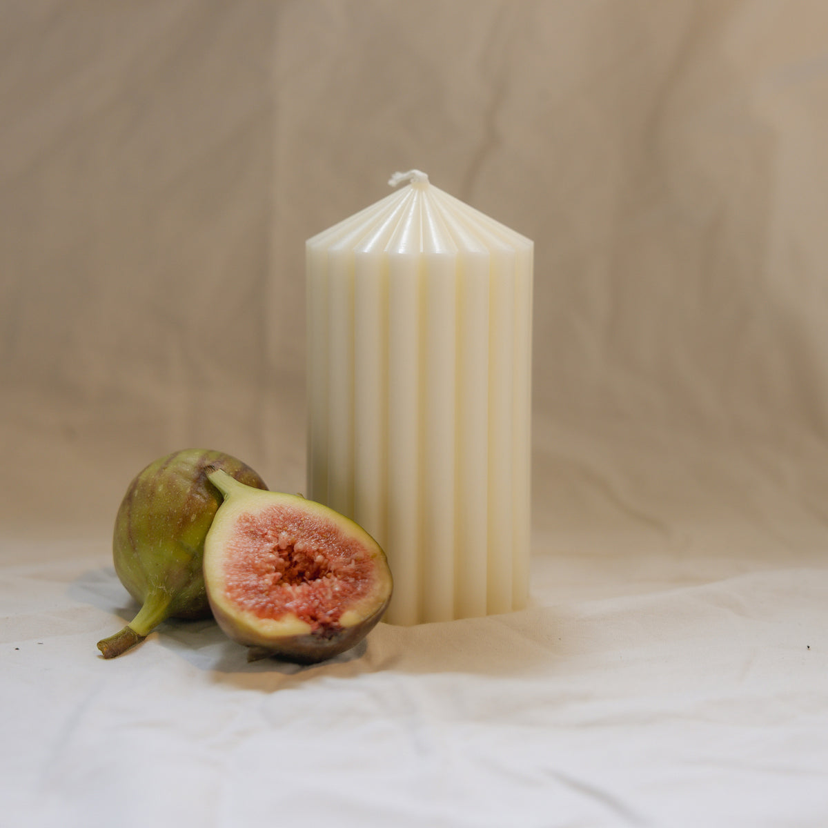 Pillar Candle II, a fluted pillar candle in beeswax and soy, unscented, beside fresh figs