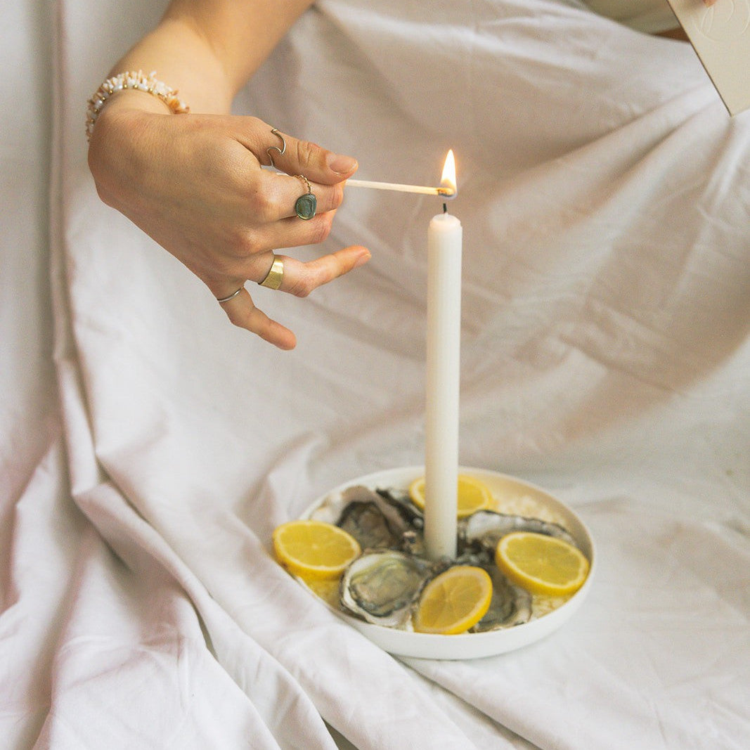 A LLIOR taper candle being lit on a dish of oysters and lemon
